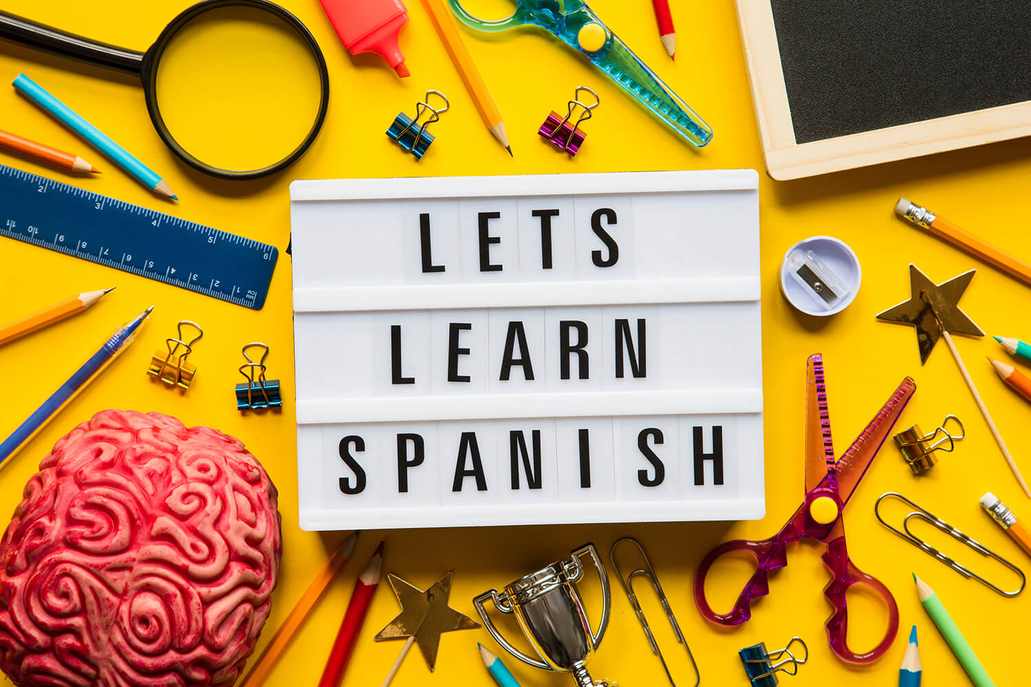 A “Let’s learn Spanish” lightbox message on a bright yellow background surrounded by school items’