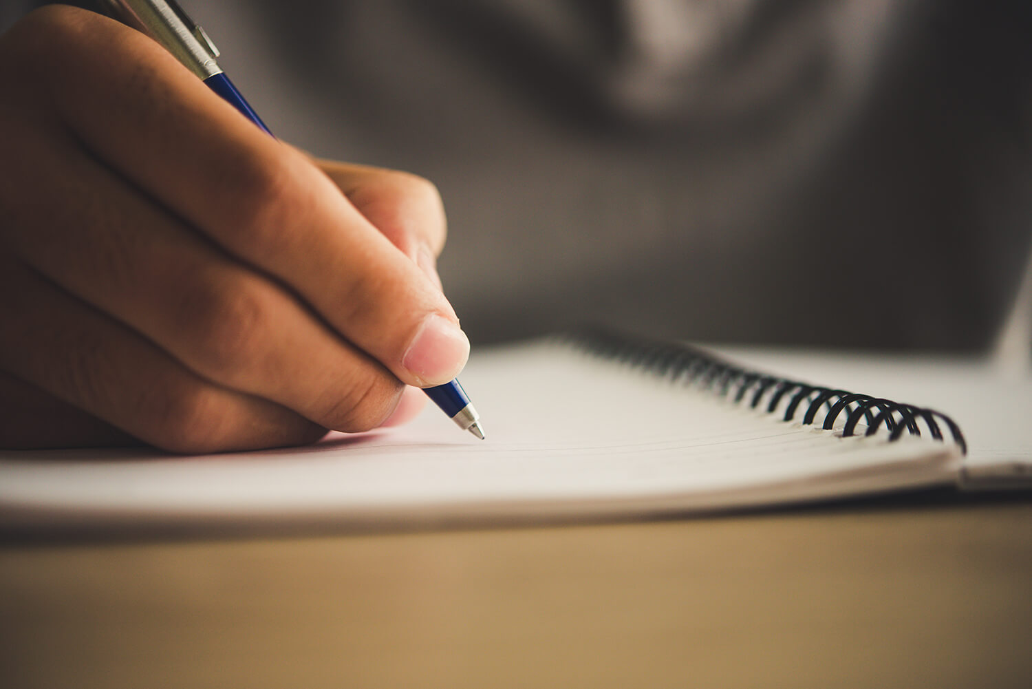 A closeup on a person’s hand writing in a notebook with a pen